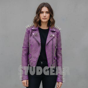 May include: A purple leather jacket with silver metal studs and spikes. The jacket has a classic biker style with a zipper closure and multiple pockets. The model is wearing a black shirt and black jeans.