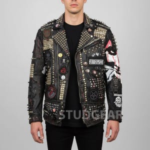 May include: Black leather jacket with gold and silver studs, spikes, and patches. The jacket features various patches with skull and other graphic designs. The text "SUB HUMAN" and "STUDGEAR" are visible on the jacket.