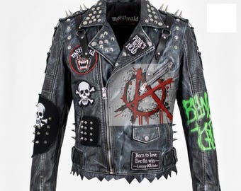 Puede incluir: Una chaqueta de cuero gris desgastado con múltiples parches, tachuelas y púas. Los parches incluyen una calavera y huesos cruzados, un lobo gruñendo y el texto "PUNK'S NOT DEAD". La chaqueta presenta un símbolo de anarquía rojo y texto verde estilo grafiti.