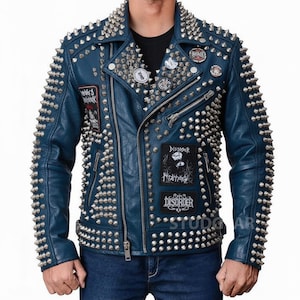 Op de afbeelding: Een blauwe leren jas met zilveren metalen kegelvormige studs op de schouders, revers en mouwen. De jas heeft meerdere patches met tekst en afbeeldingen en een ritssluiting. Een klassieke biker-stijl.