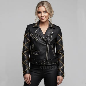 May include: Black leather jacket with gold studs on the shoulders, sleeves, and collar. The jacket has a zipper closure, a belt, and the word "STUDGEA" printed on the belt. The jacket is a classic biker style.