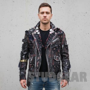 Può includere: Giacca di pelle nera con un'estetica punk rock usurata. La giacca presenta borchie metalliche, toppe e dettagli di cuciture rosse. Ha un colletto a revers e più tasche. La giacca è indossata sopra una maglietta nera e jeans blu.
