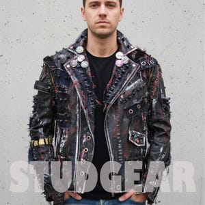 Puede incluir: Chaqueta de cuero negra con costuras rojas y blancas, tachuelas metálicas y parches. La chaqueta tiene cierre de cremallera, múltiples bolsillos y botones decorativos. La palabra "STUDGEAR" es visible en la parte inferior de la imagen.