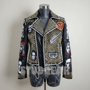May include: Black leather jacket with gold-colored studs and white trim. The jacket features multiple patches with portraits and a red and gold patch on the upper chest. The jacket has a zipper closure and a notched collar.