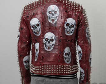 Puede incluir: Chaqueta de cuero burdeos adornada con múltiples diseños de calaveras blancas con ojos rojos. La chaqueta presenta púas metálicas plateadas en los hombros, el cuello y la cintura. Cierre de cremallera y dobladillo a rayas blancas y negras.