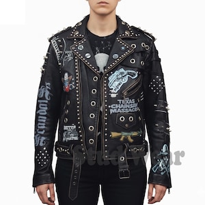 May include: Black leather jacket with silver studs, spikes, and patches. Features the text "Texas Chainsaw Massacre" and "Scandal". Includes a belt and multiple pockets. A bold, edgy fashion statement.