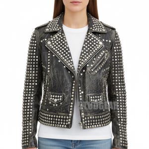 May include: A black distressed leather jacket adorned with silver studs. The jacket has an asymmetrical zip, pockets, and stud detailing on the collar, shoulders, and sleeves. It is worn over a white t-shirt, showcasing a classic biker style.