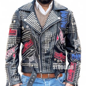 May include: Black leather jacket adorned with silver studs and patches. The jacket has a classic biker design with a notched collar, asymmetrical zip, and a waist belt. Patches with text and graphics are sewn onto the jacket.