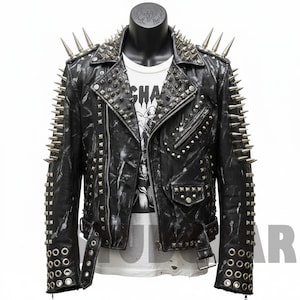 Op de afbeelding: Zwarte leren jas met zilveren spikes op de schouders, kraag en mouwen. De jas heeft een ritssluiting, meerdere zakken en zilveren studs. Een wit grafisch t-shirt is eronder zichtbaar.