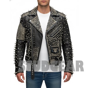 Op de afbeelding: Zwarte leren jas met zilveren metalen studs en spikes. De jas heeft een asymmetrische ritssluiting, een reverskraag en een riem in de taille. De mouwen en schouders zijn zwaar bezaaid met studs. Het woord "STUDGEAR" staat onderaan de jas.