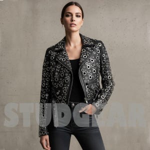 May include: Black leather jacket with silver eyelets. The jacket features a classic biker design with a notched collar, an asymmetrical zip, and several pockets. The eyelets are evenly spaced across the jacket, creating a distinctive and edgy appearance. The model is wearing black jeans and a black top.