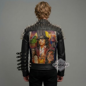 Puede incluir: Chaqueta de cuero negro con púas plateadas en los hombros y un diseño pintado colorido en la espalda. El diseño presenta un retrato de una persona con sombrero de copa y otras figuras. La chaqueta tiene múltiples correas en las mangas.