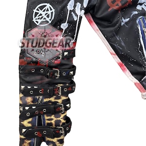 May include: A black jacket sleeve featuring white paint splatters, a pentagram symbol, and multiple black buckled straps with silver-tone studs. The lower portion displays a leopard print pattern and a vertical zip. The text STUDGEAR is visible.
