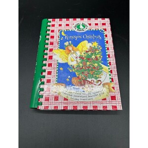 Puede incluir: Un libro de cocina encuadernado en espiral titulado "Homespun Christmas" con una cubierta a cuadros rojos y blancos. La portada presenta una ilustración de un ángel decorando un árbol de Navidad. El libro tiene una lomo verde e incluye texto sobre recetas familiares y tradiciones navideñas.