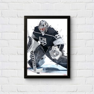 Può includere: Stampa incorniciata ad acquerello di un portiere di hockey in uniforme bianca e nera con il numero 32. Il portiere è in posizione difensiva, con il logo dei Kings di Los Angeles visibile. L'opera d'arte ha un effetto splash.