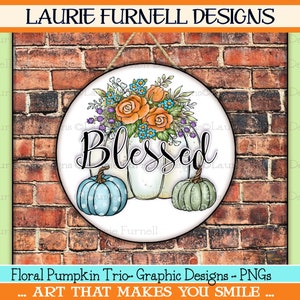 May include: A round, white sign with a floral arrangement of orange, blue, and purple flowers. The sign says "Blessed" in black script and features three pumpkins, one blue, one white, and one green. The sign is hanging on a brick wall.