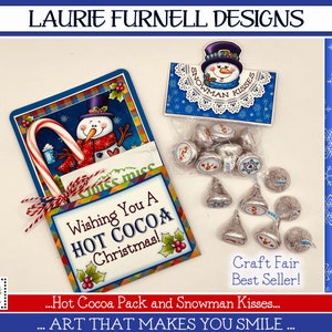 May include: A Christmas-themed gift set featuring a red and white candy cane, a small cup of hot cocoa, and a snowman with a red scarf. The set is packaged in a colorful card with the text "Wishing You A HOT COCOA Christmas!" and a separate card with a snowman and the text "Snowman Kisses".