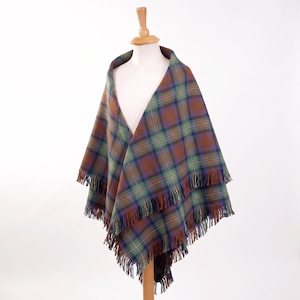 May include: A plaid shawl featuring a tartan pattern in shades of brown, green, and blue. The fabric has a soft texture and is finished with long, fringed edges along the bottom hem, draped over a mannequin to display the woven design.