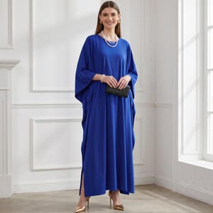 May include: A cobalt blue caftan dress with wide sleeves and side slits. The dress is paired with gold heels and a black clutch. The person is wearing a pearl necklace and bracelet.