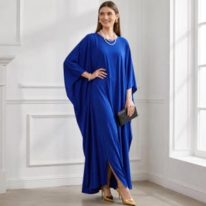 May include: A long, flowing cobalt blue dress with wide sleeves and a side slit. The dress is paired with gold heels and a small black clutch. The model is also wearing a pearl necklace and bracelet.