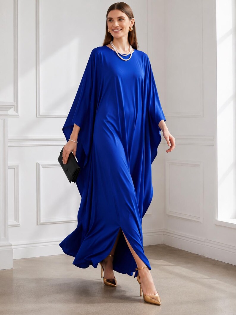 May include: A flowing, cobalt blue caftan dress with wide sleeves and a high side slit. The dress is paired with gold-colored high heels and a black clutch. The model is also wearing a pearl necklace and earrings.