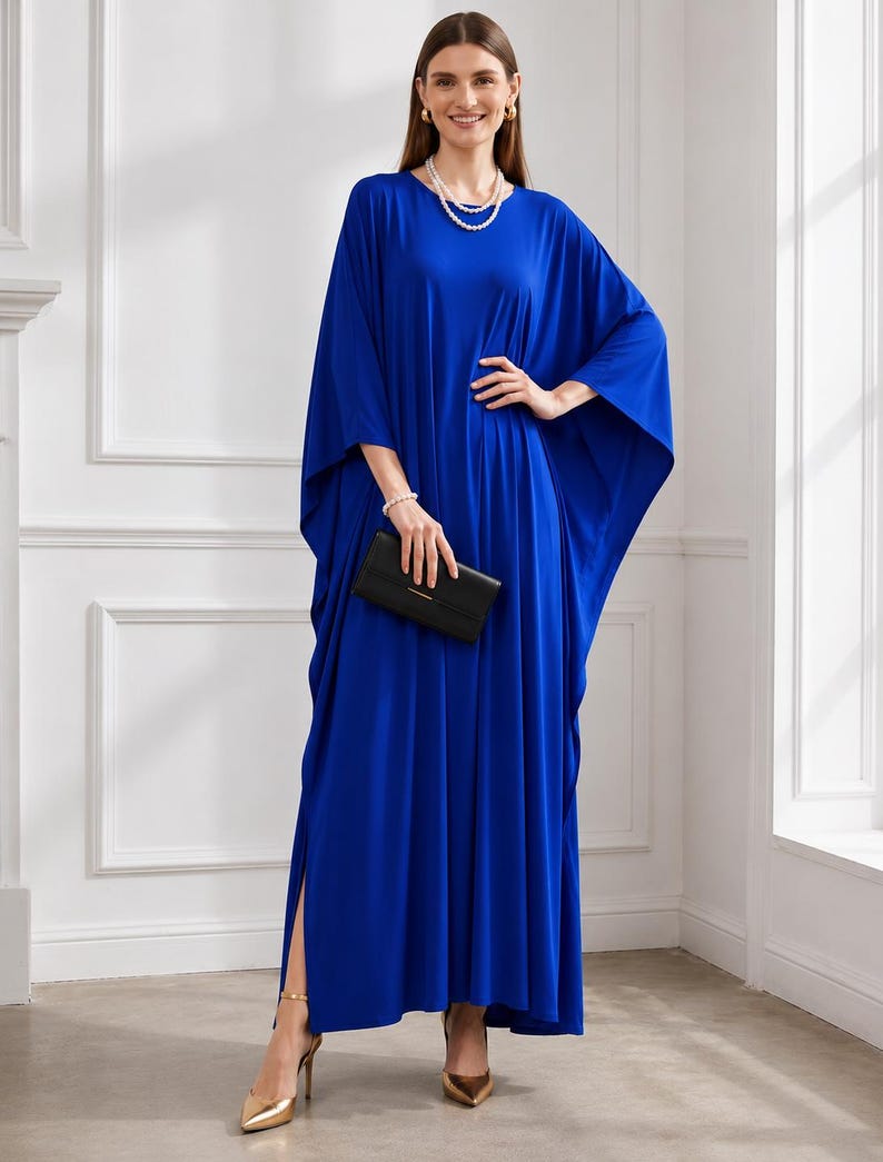 May include: A long, flowing cobalt blue dress with wide sleeves and a high side slit. The dress is accessorized with a pearl necklace, bracelet, and gold heels. A black clutch is held in the hand.