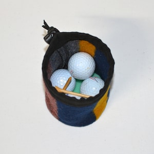May include: A blue, yellow, and red golf ball holder with a zipper closure. The holder is filled with three white golf balls and a wooden tee.