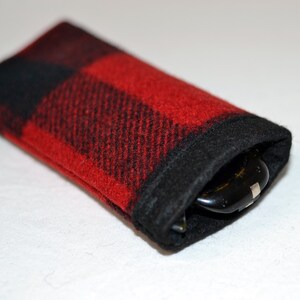 K&ouml;nnte beinhalten: Rechteckiges Brillenetui aus rot-schwarz kariertem Stoff. Der Rand der &Ouml;ffnung ist schwarz. Das Etui enth&auml;lt eine Brille. Das Etui ist weich und hat eine lebendige Farbe.
