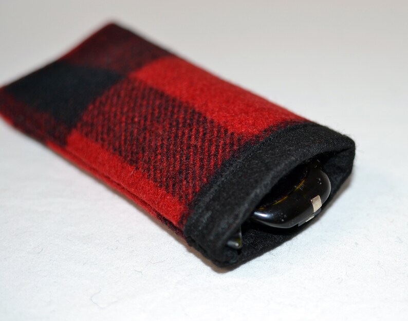 K&ouml;nnte beinhalten: Rechteckiges Brillenetui aus rot-schwarz kariertem Stoff. Der Rand der &Ouml;ffnung ist schwarz. Das Etui enth&auml;lt eine Brille. Das Etui ist weich und hat eine lebendige Farbe.