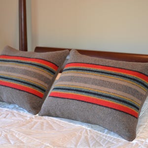May include: Two gray striped throw pillows with red, yellow, and blue accents on a white bed.