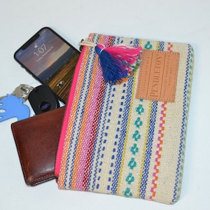 May include: A multi-colored striped zippered pouch with a brown leather patch that says "PENDLETON" and a blue and pink tassel. The pouch is filled with a smartphone, a wallet, and keys.