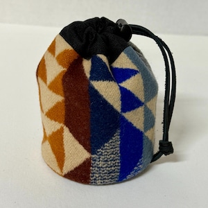 May include: A small drawstring pouch featuring a geometric pattern in shades of mustard yellow, dark brown, navy blue, light blue, and cream. The bag has a black fabric top closure with a black plastic cord lock and a black leather drawstring cord.