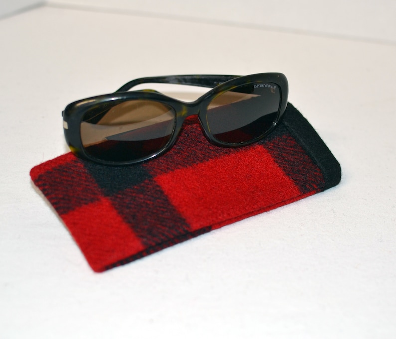 K&ouml;nnte beinhalten: Sonnenbrille mit Schildpattrahmen und dunklen Gl&auml;sern liegen auf einem rot-schwarz karierten Brillenetui. Das Etui besteht aus einem weichen, strukturierten Stoff.