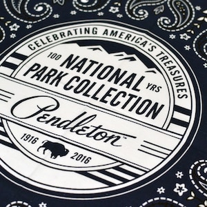 May include: A blue bandana with a white circle in the center. The circle has the text "Celebrating America's Treasures 100 YRS National Park Collection Pendleton 1916 2016" in a black font.