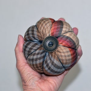 May include: A brown and red plaid fabric pincushion with a decorative metal button in the center.