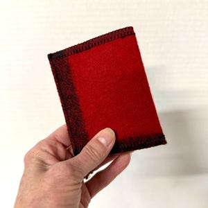May include: A rectangular red felt item with black stitching around the edges. The felt has a gradient effect, transitioning from red to black on one side. The item is held in a hand.