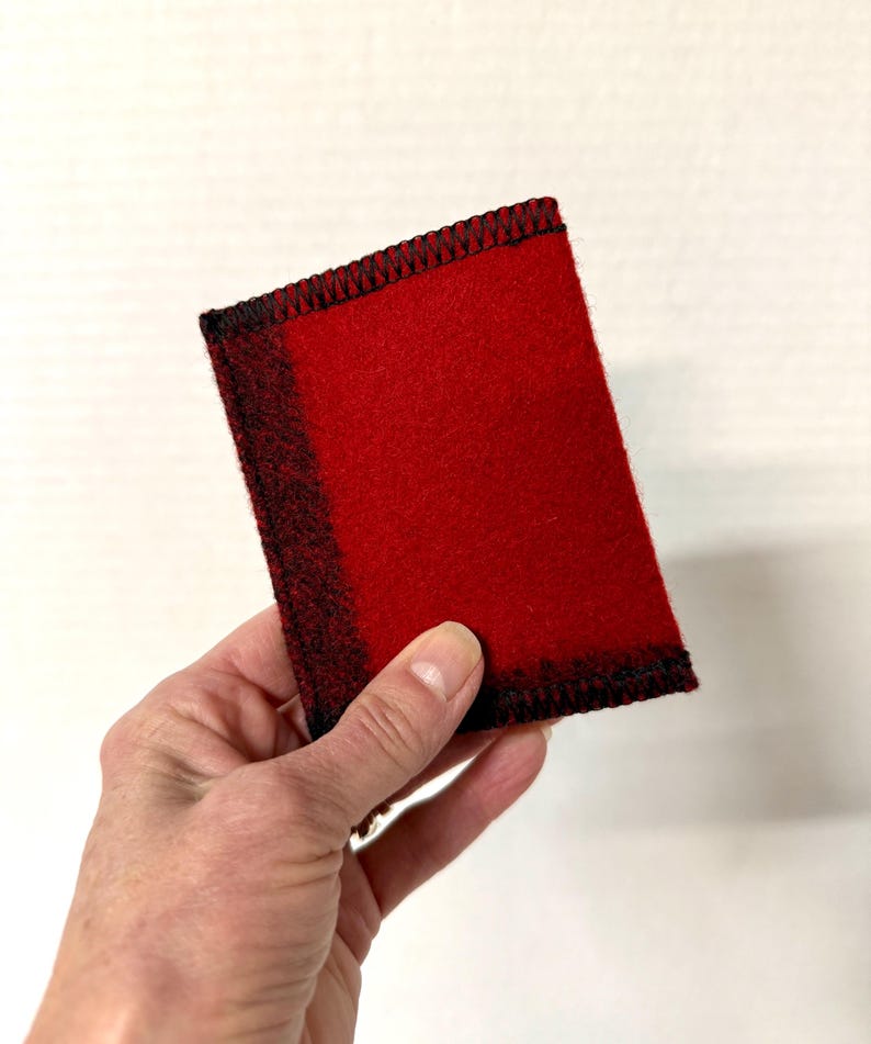May include: A rectangular red felt item with black stitching around the edges. The felt has a gradient effect, transitioning from red to black on one side. The item is held in a hand.