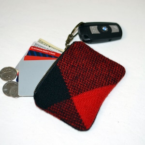 May include: A small red and black zippered pouch with a key chain attached. The pouch is filled with credit cards and coins.