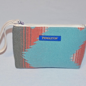 May include: A small blue, gray, and orange patterned zippered pouch with a white handle. The pouch has a blue label with the text "PENDLETON" in gold lettering.