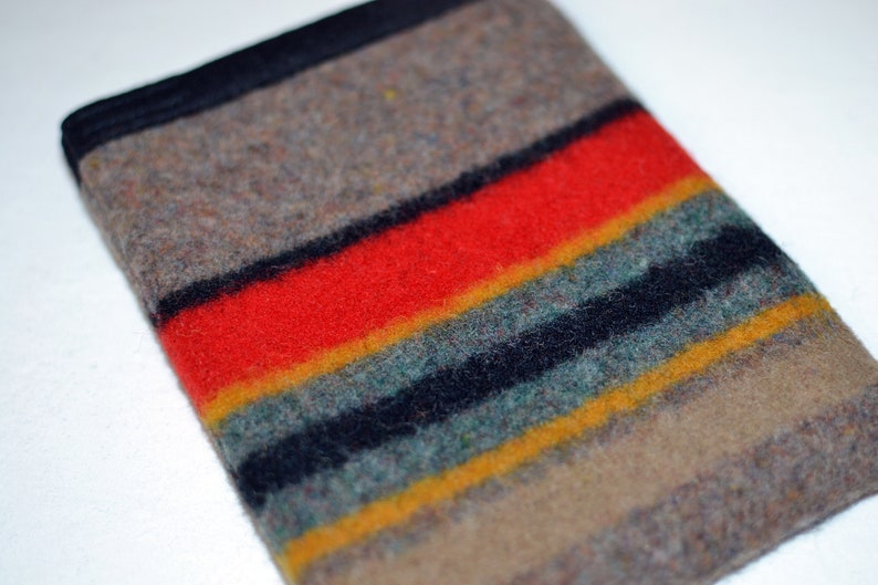 May include: A brown, black, red, yellow, and green striped wool blanket. The blanket is folded in half and has a black border.
