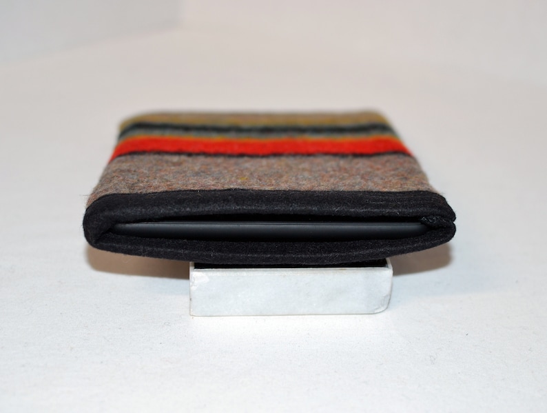 May include: A black felt case with a colorful striped pattern. The case is folded closed and sitting on a white surface.
