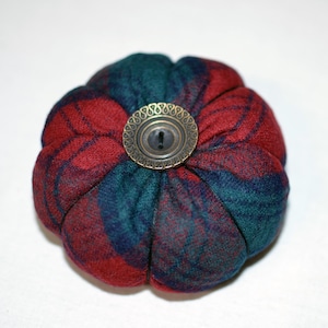 May include: A red and green plaid pincushion with a round, brass button in the center.