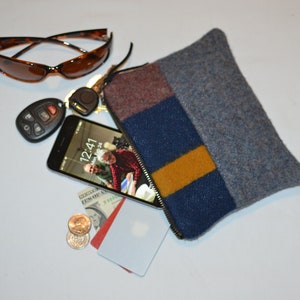 May include: A gray felt zippered pouch with a blue, yellow, and red striped design. The pouch is open and contains a smartphone, keys, credit cards, and coins.