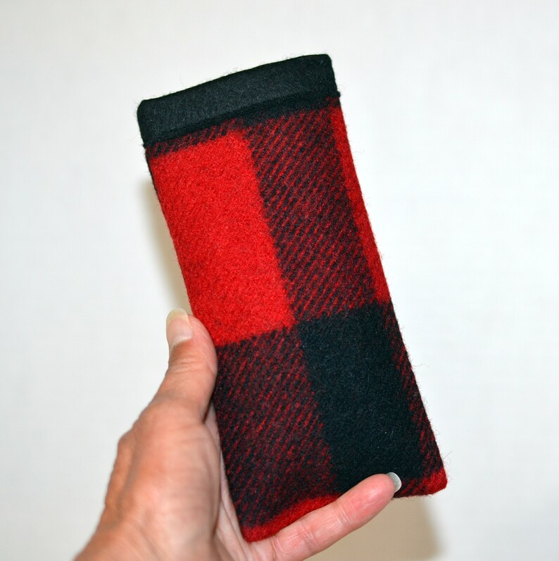 K&ouml;nnte beinhalten: Ein rechteckiges Brillenetui mit einem rot-schwarzen Karomuster. Das Etui besteht aus einem weichen, filzartigen Material und hat eine durchgehend schwarze Oberseite. Das Etui wird in einer Hand gehalten.