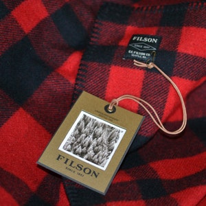 May include: Red and black plaid blanket with a brown tag that says "Filson Since 1897" and a smaller tag that says "Filson Since 1897 C.C. Filson Co. Seattle, WA."