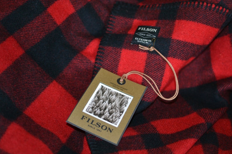 May include: Red and black plaid blanket with a brown tag that says "Filson Since 1897" and a smaller tag that says "Filson Since 1897 C.C. Filson Co. Seattle, WA."