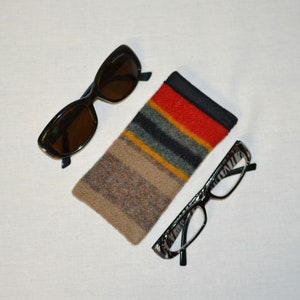 May include: An assortment of eyewear and accessories. Includes a pair of dark brown sunglasses, a pair of eyeglasses with a black and white pattern, and a colorful striped glasses case. The case features red, yellow, and green stripes.