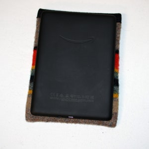 May include: A black e-reader with a gray fabric case. The case has a colorful striped pattern with red, yellow, blue, and gray stripes. The e-reader has the Amazon logo on the front.