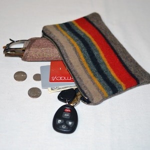 May include: A striped gray, red, yellow, and blue zippered pouch with a key chain, a credit card, and a pair of glasses inside.