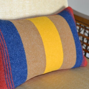 May include: A striped throw pillow with red, blue, yellow, and brown stripes. The pillow is made of a soft, textured fabric.